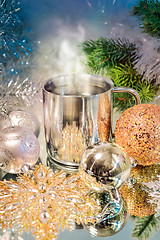 Image showing Metal mug with hot steaming coffee, Christmas balls, Christmas tree.