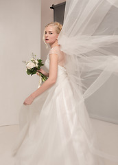 Image showing Bride in beautiful dress standing indoors in white studio interior like at home. Trendy wedding style shot. Young attractive caucasian model like a bride tender looking.