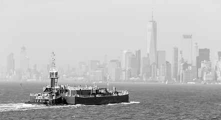 Image showing Freight tug pushing cargo ship to the port in New York City and Lower Manhattan skyscarpers skyline in background.