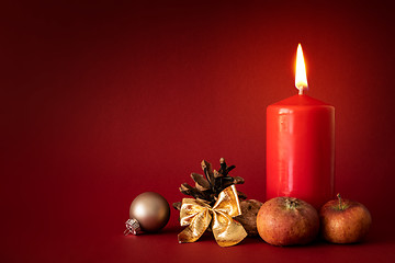 Image showing Christmas decoration with a burning candle on red background