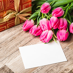 Image showing Beautiful bouquet from pink tulips and a gift on a table