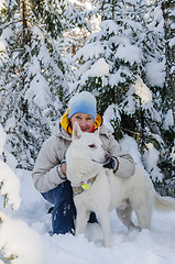 Image showing Joyful woman with a white dog in the winter snow-covered forest