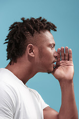 Image showing The young Afro-American man whispering a secret behind her hand over blue background