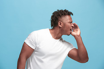 Image showing The young afro-american man whispering a secret behind her hand over blue background