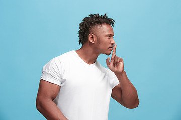 Image showing The young afro-american man whispering a secret behind her hand over blue background