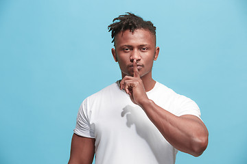 Image showing The young afro-american man whispering a secret behind her hand over blue background