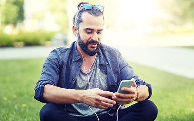 Image showing man with earphones and smartphone sitting on grass