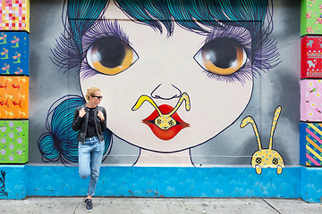 Image showing Woman talking on smartphone leaning against colorful graffiti wall in New York city, USA.