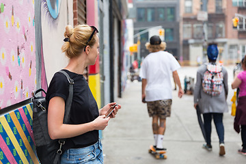 Image showing Woman using smartphone against colorful graffiti wall in New York city, USA.