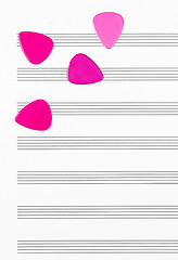 Image showing Crimson guitar picks on empty sheet music paper