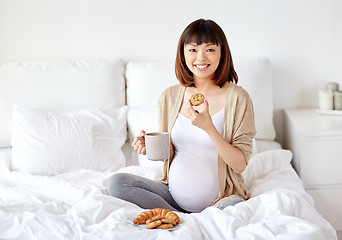 Image showing happy pregnant woman eating cookie in bed at home