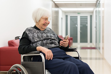 Image showing Lonley elderly 95 years old woman sitting at the wheelchair using modern mobile phone.