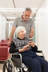 Image showing Middle aged man showing and helping elderly 95 years old woman sitting at the wheelchair how to use modern mobile phone.