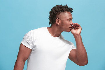 Image showing The young afro-american man whispering a secret behind her hand over blue background