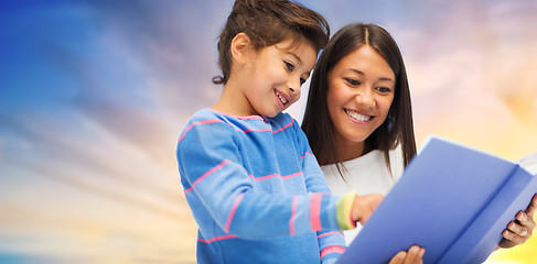 Image showing happy mother and daughter reading book over sky