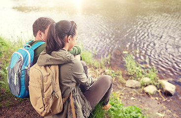 Image showing couple with backpacks sitting on river bank