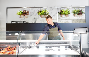 Image showing male seller adding ice to fridge at fish shop