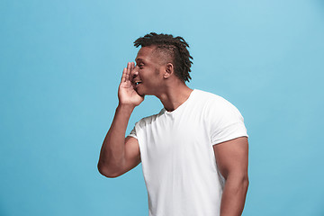 Image showing The young afro-american man whispering a secret behind her hand over blue background