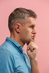 Image showing The young man whispering a secret behind her hand over pink background