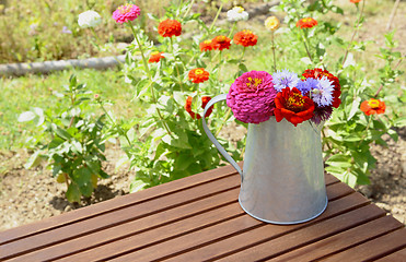 Image showing Arrangement of zinnias and cornflowers in a metal jug outdoors