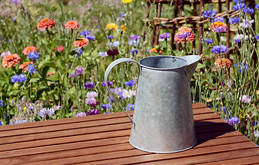 Image showing Empty metal pitcher on a table in a flower garden