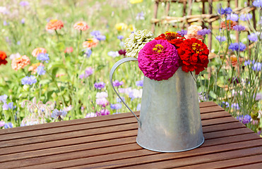 Image showing Zinnias in a rustic pitcher on a garden table