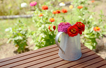 Image showing Rustic pitcher holding zinnia flowers on a garden table