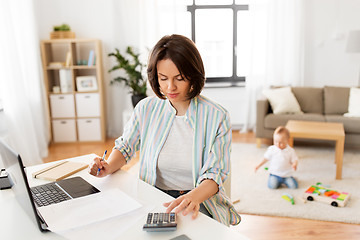 Image showing working mother counting on calculator and baby