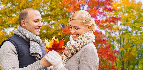 Image showing smiling couple with maple leaves in autumn park