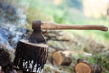 Image showing Axe in tree stump and smoke from campfire