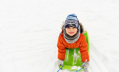 Image showing happy little boy riding sled on snow in winter