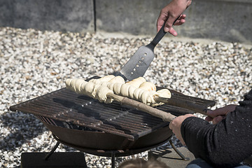 Image showing Dough on a grill wrapped around wooden sticks