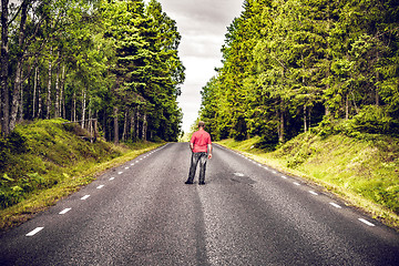 Image showing Man in a red shirt looking down an asphalt road