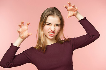 Image showing Angry, playful and scares woman is teaseing on the pink studio background and looking at camera