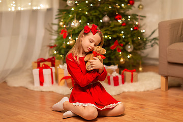 Image showing girl in red dress hugging teddy bear at home