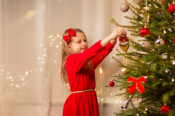 Image showing happy girl in red dress decorating christmas tree