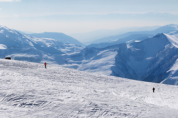 Image showing Two skiers downhill on snow off-piste slope and mountains in haz