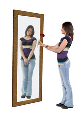 Image showing Young woman giving a flower to her reflection in a mirror