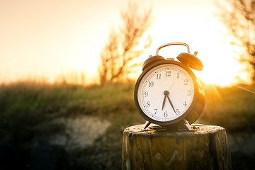 Image showing Alarm clock on a wooden post in the morning sunrise