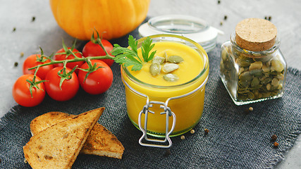 Image showing Creamy pumpkin soup in jar with bread and tomatoes