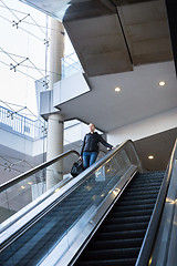 Image showing Businesswoman with large black bag and mobile phone descending on escalator.