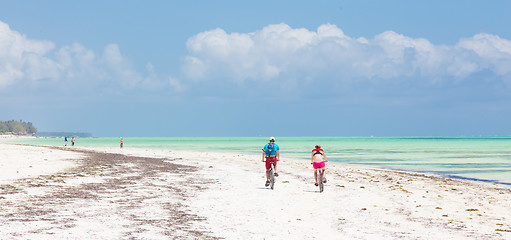 Image showing Active sporty tourist couple cycling down picture perfect white sand tropical beach of Paje, Zanzibar, Tanzania.