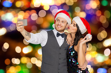 Image showing couple in santa hats taking selfie at christmas