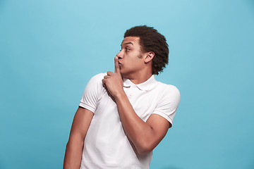 Image showing The young man whispering a secret behind her hand over blue background