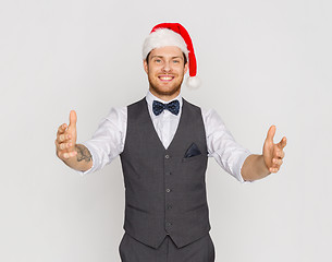 Image showing happy man in santa hat holding something imaginary