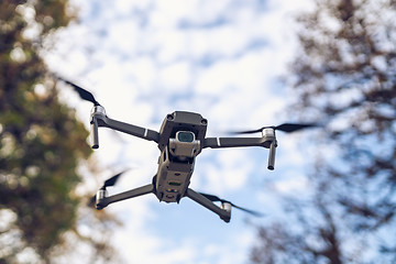 Image showing Drone flying in the air, visible trees and blue sky above