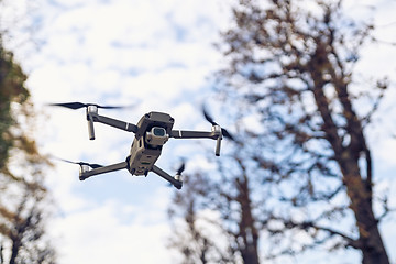 Image showing Drone flying in the air, visible trees and blue sky above