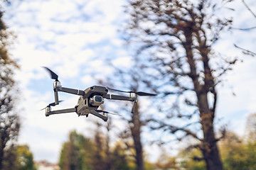 Image showing Drone flying in the air, visible trees and blue sky above