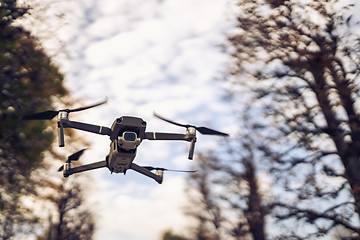 Image showing Drone flying in the air, visible trees and blue sky above