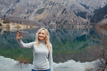 Image showing Smiling woman makes selfie at the mountain lake